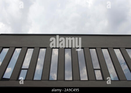 Vista dal basso di un edificio moderno e le sue finestre che riflettono le nuvole in cielo. Foto Stock