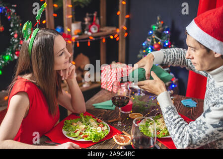 Un giovane bella coppia di amanti trascorrere una serata festiva cenare e bere il vino da occhiali nelle decorazioni di Natale per la vigilia di capodanno. Foto Stock