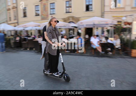 Cracovia. Cracovia. La Polonia. Giovane donna e giovane uomo alla guida di scooter elettrico. Piazza del Mercato nel centro della Città Vecchia. Motion Blur. Foto Stock