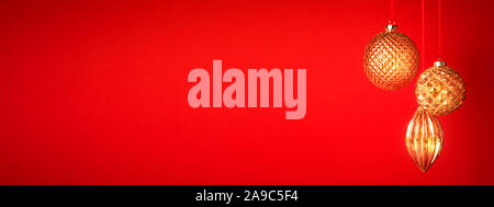 Tre golden baubles di Natale appeso contro lo sfondo rosso. Anno nuovo banner. Messa a fuoco selettiva. Foto Stock