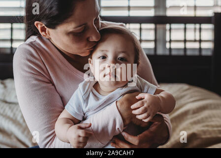 Amare mid-30â€™s mom cuddling bambina sul giro in camera da letto vicino alla finestra Foto Stock