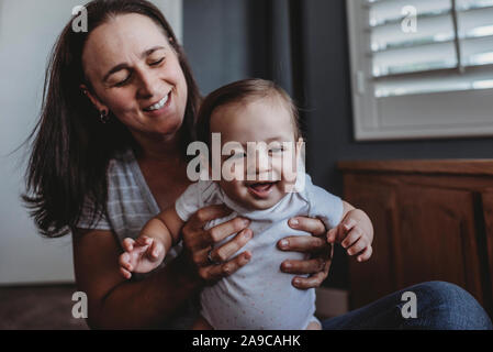 Sorridente mom con capelli lunghi aiutando Laughing baby stand Foto Stock