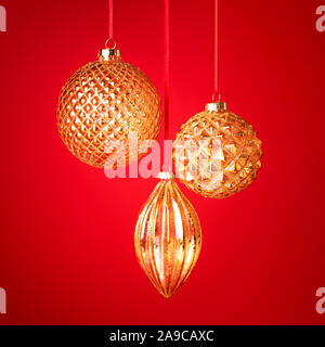 Tre golden baubles di Natale appeso contro lo sfondo rosso. Anno nuovo bigliettino. Messa a fuoco selettiva. Foto Stock