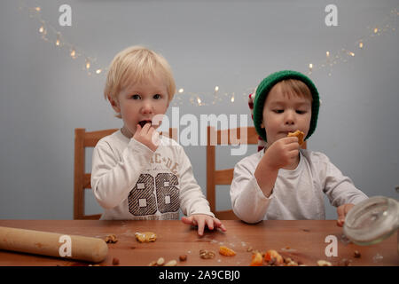 Due ragazzi di mangiare i cookie nel tempo di Natale, uno indossa elf hat, lo stile di vita Foto Stock