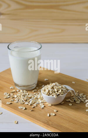 I fiocchi d'avena e un bicchiere di latte di avena su uno sfondo di legno Foto Stock