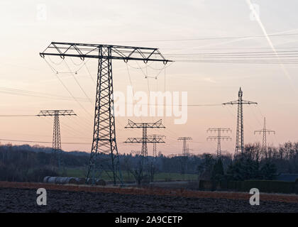 Grande raccolta di tralicci di energia elettrica con i cavi, essi sono sfalsati come sagome di fronte un lievemente colorata del cielo della sera nella zona in prossimità di un bi Foto Stock