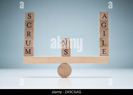 Equilibrio di legno Vs SCRUM Agile blocchi su altalena oltre la scrivania contro sfondo blu Foto Stock