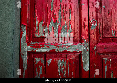 Closeup texture dettagliate di colore rosso brillante vernice scrostata off di una vecchia porta di legno. Panno insinuato in attraverso le crepe nelle pareti. Foto Stock