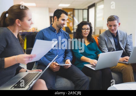 Un gruppo di persone in ufficio a lavorare e a discutere insieme con i computer, riunione del team del progetto circa la strategia, i collaboratori si aiuta a vicenda con creat Foto Stock