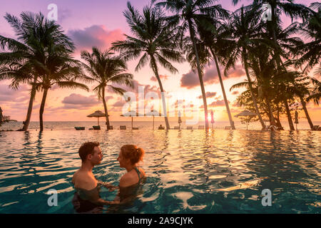 Coppia al beach vacation resort di vacanza rilassante in piscina con scenic paesaggio tropicale al tramonto, estate romantica luna di miele isola destinat Foto Stock