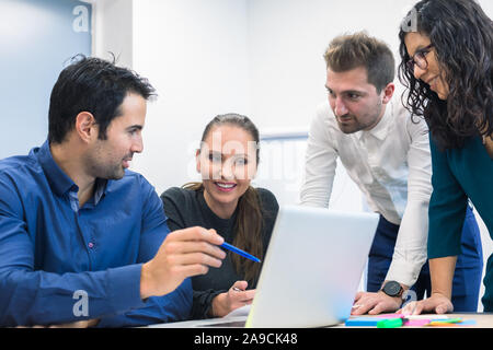 Un gruppo di uomini di affari che discutere le idee e strategia in sala riunioni, donna sorridente, più etnicità, leadership, computer sul tavolo per ufficio Foto Stock