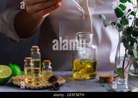 La donna versa manualmente eucalipto olio essenziale nella bottiglia sul tavolo grigio Foto Stock