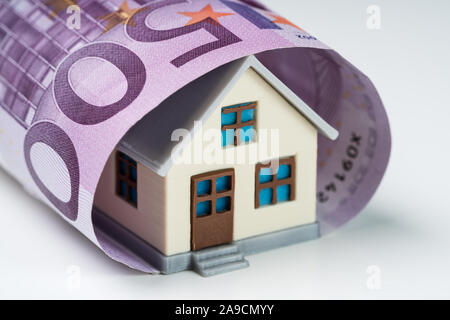 Close-up di 500 Euro nota coperto con casa in miniatura contro uno sfondo bianco Foto Stock