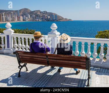 Un giovane seduto su una panchina a Placa del Castell affacciato sulla spiaggia di Levante a Benidorm, Spagna. Foto Stock