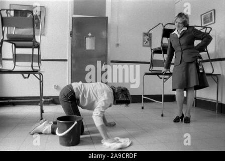 Lavoratrice prigioniera e guardia. HM Prison Styal Wilmslow Cheshire Regno Unito anni '1980 Prigione femminile delle donne detenuta, guardia carceraria l'agente in piedi sopra una prigioniera donna che sta pulendo il pavimento. Cheshire 1986 Inghilterra HOMER SYKES Foto Stock