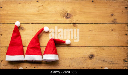 Una immagine di tre rossi Santa Claus cappelli con sfondo di legno Foto Stock