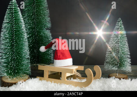 Decorazione di natale con un rosso di Santa Claus hat su una slitta a fianco di abeti e bagliore leggero Foto Stock