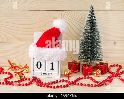 Santa Claus Red Hat su un di legno bianco calendario perpetuo con data 01 gennaio. Albero di natale e cordone rosso garland su un naturale sfondo di legno. Foto Stock
