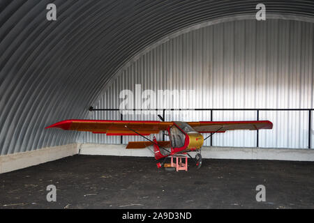 Molto piccolo singolo posto ultralight glider sorge in un angolo di un hangar in metallo. Foto Stock