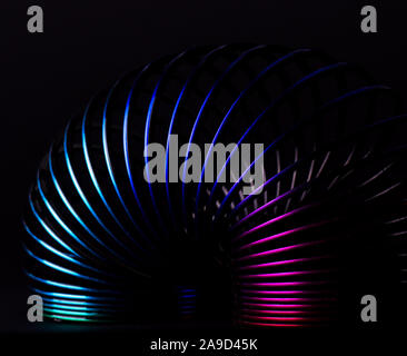 La molla Slinky rainbow allungando il giocattolo contro uno sfondo scuro. Abstract sfondo multicolore buona per il walpaper e screen saver del telefono. Foto Stock
