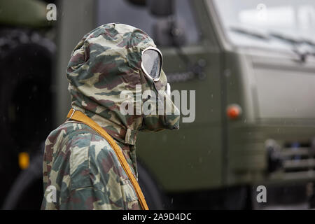Manichino vestito in un camuffamento speciale protezione chimica tuta e maschera a gas si erge sullo sfondo di un camion militare Foto Stock