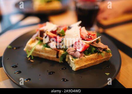 Waffle sandwich con pancetta e pollo Insalata frech sulla piastra nera. Sullo sfondo di un tavolo di legno Foto Stock