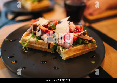 Waffle sandwich con pancetta e pollo Insalata frech sulla piastra nera. Sullo sfondo di un tavolo di legno Foto Stock