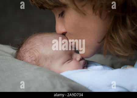 Cuddling madre con bambino, kissing baby di fronte, sfondo scuro Foto Stock