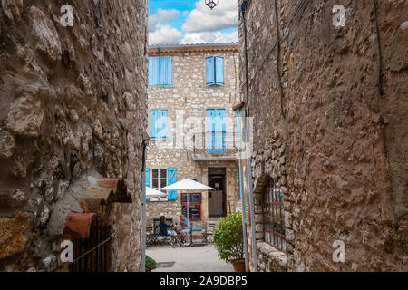 Un giovane mangia il pranzo sulla terrazza di un cafè sul marciapiede sotto il francese persiane blu nello storico borgo medievale di Gourdon Francia Foto Stock