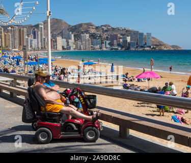 Benidorm, Spagna - 13 Aprile 2019: una coppia sulla mobilità scooter seduti lungo la passeggiata sulla spiaggia di Levante nella famosa città di Benidorm in Spagna. Foto Stock