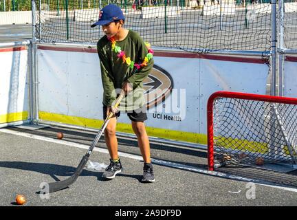 Ragazzo gioca street hockey su asfalto. Lui è di indossare scarpe da tennis, una maglietta oversize, pantaloncini, un cappello da baseball e un colorato lei intorno al suo collo. Foto Stock