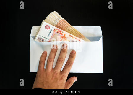 Grandi denominazioni di 5000 rubli in una busta bianca. Un man mano trattiene una busta con il denaro. il concetto di concussione e corruzione. contanti, del flusso di cassa Foto Stock