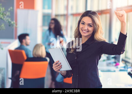 Ritratto di felice imprenditrice azienda digitale compressa in ufficio in piedi di fronte a colleghi che hanno discusso a sfondo Foto Stock