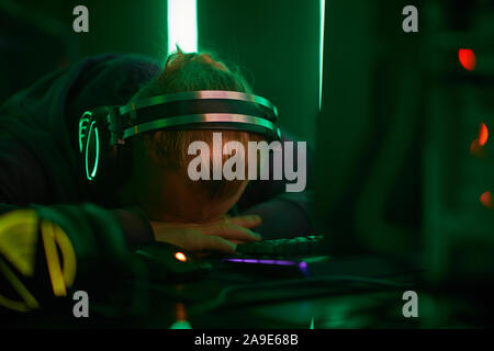 Giovane programmatore di computer nelle cuffie sdraiato su un tavolo e dormire egli stanco dopo il lavoro Foto Stock