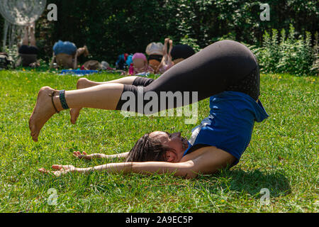 Una vista ravvicinata di una giovane donna caucasica la pratica dello yoga, diverse persone godersi l'esterno sessione di yoga in background durante il raduno spirituale Foto Stock