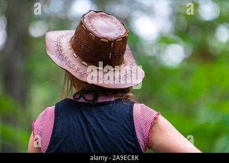 Messa a fuoco selettiva close up sulla vista posteriore della donna che indossa il cowboy Cappello in cuoio come ella guardando avanti, con copia di spazio e di sfocare lo sfondo della natura Foto Stock