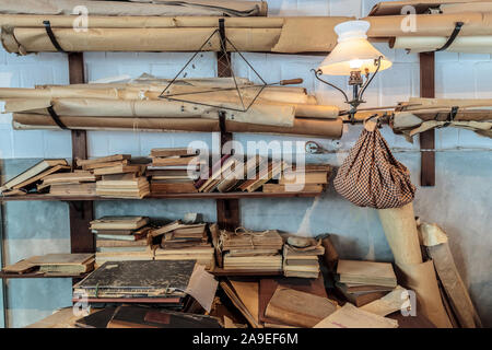 Vecchio studyrrom con pareti blu pieno di libri degradato e rotoli di carta pergamena Foto Stock