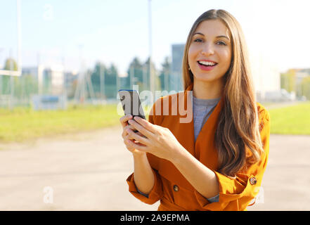 Ritratto di happy business donna che guarda la telecamera tenendo premuto smart phone all'aperto. Foto Stock