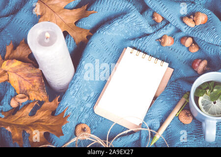 Composizione d'autunno. Tazza di tae, blanket, notebook con penna, autunno foglie essiccate, candela e acorn. Appartamento laico, vista dall'alto, spazio di copia Foto Stock