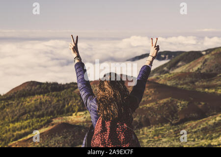 Adolescente con zaino e le mani alzate in piedi sulla cima della montagna con splendida vista a mare della foresta e le nuvole. Vulcano Teide Tenerife, Spagna. Foto Stock