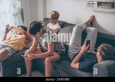 Gruppo di adolescente utilizza lo smartphone seduto su un divano a casa. Giovani ragazzi e una ragazza la condivisione di foto e video guarda la storia sociale online. Amici godeteveli Foto Stock