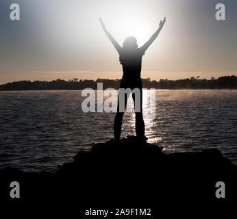 Donna con le braccia sollevate in controluce Foto Stock