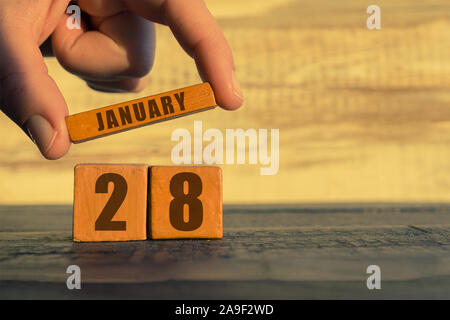 Gennaio 28th. Il giorno 28 del mese, il calendario su un cubo di legno. Una donna mette a mano il nome del mese sul numero del mese su uno sfondo di legno Foto Stock