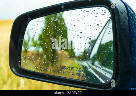 Specchietto retrovisore con gocce di acqua e paesaggio rurale. Il fuoco selettivo DOF poco profondo Foto Stock