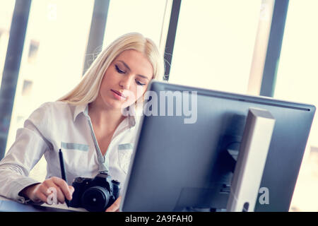 Fotografo professionista seduto alla sua scrivania in ufficio che guarda lontano e sorridente. Foto Stock