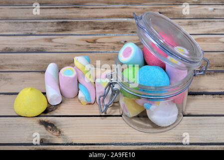 Marshmallows colorati in un vasetto di vetro su uno sfondo di legno Foto Stock