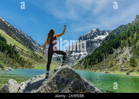 Donna in posa di vittoria su una roccia ad un lago di montagna Foto Stock