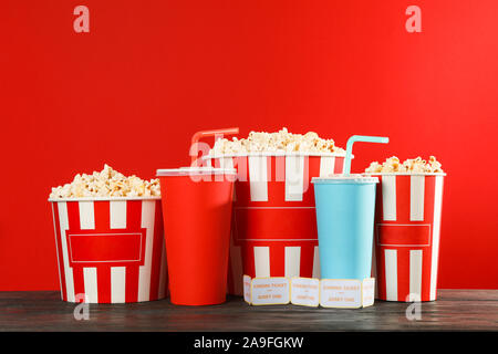 Secchielli per popcorn, bicchieri di carta e biglietti contro lo sfondo di colore rosso, lo spazio per il testo Foto Stock