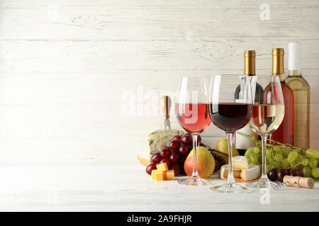 Frutta, formaggio, bottiglie e bicchieri di vino diverso su sfondo bianco, spazio per il testo Foto Stock