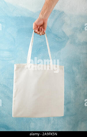 Maschio di mano azienda tote bag contro sfondo blu, spazio di copia Foto Stock